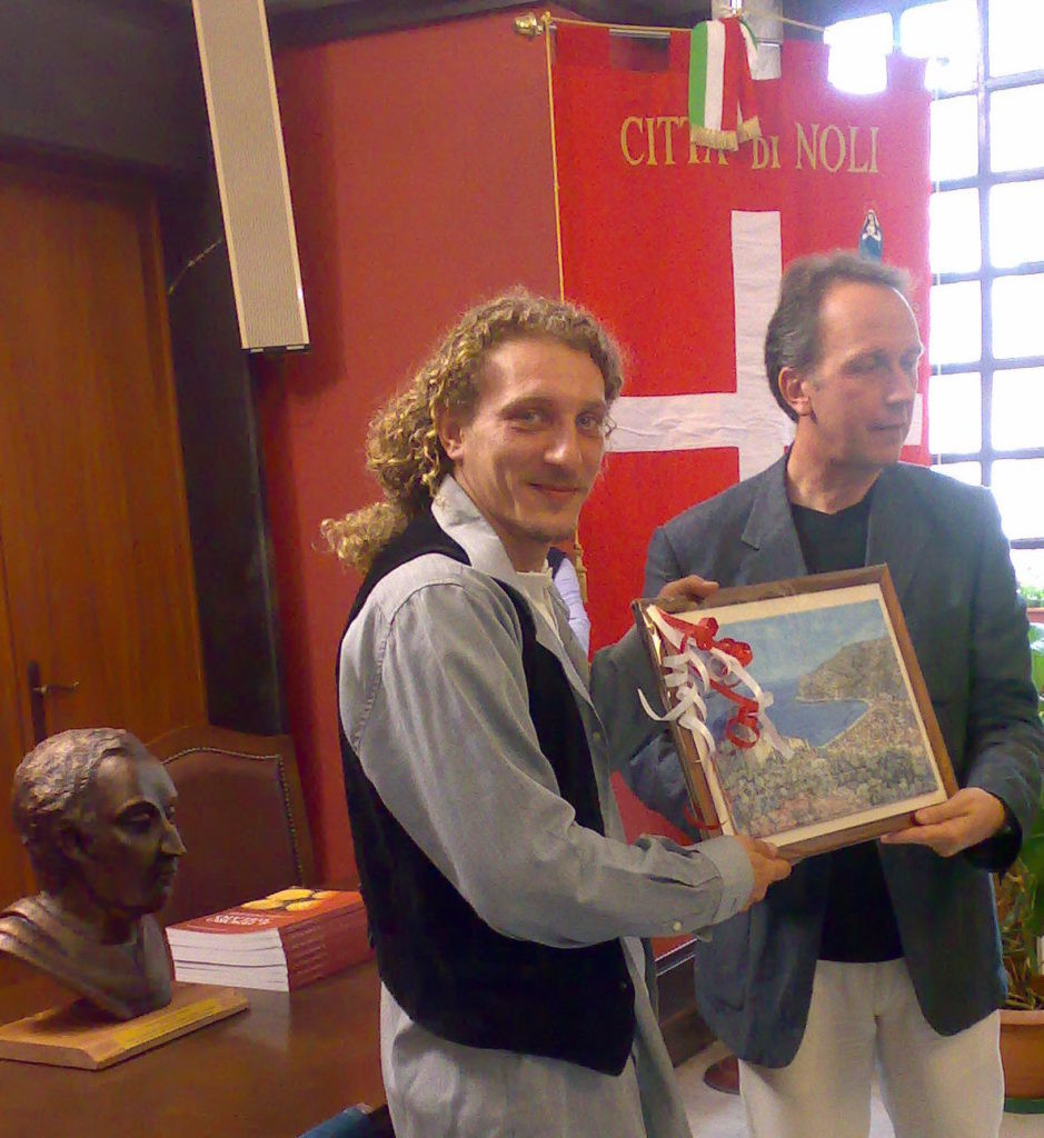 PREMIO-COLOMBO-NOLI-LAssessore-alla-cultura-e-vice-sindaco-di-Noli-ringrazia-lo-scultore-Claudio-Caporaso-autore-della-scultura-donata-come-Premio-939×1024